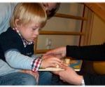 Das Bild zeigt einen kleinen Jungen, der mit einem Holz-Puzzle spielt.