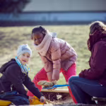 Das Bild zeigt zwei Kinder und eine Betreierin beim Spielen auf dem Außengelände.