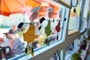 Das Bild zeigt eine bunte Fensterdekoration mit tanzenden Kühen.