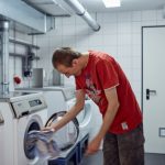 Das Bild zeigt einen jungen Mann, der Wäsche in eine Waschmaschine steckt.