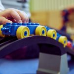 Das Bild zeigt eine Kinderhand, die einen Lego-Zug über eine Brücke fahren lässt.