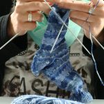 Das Bild zeigt die Hände einer Mitarbeiterin, die einen gemusterten Socken strickt.