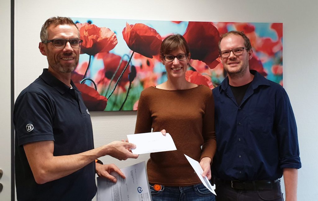 Auf dem Bild ist zu sehen, wie Frank Blasey von der Firma ZF den Spendenscheck an Christina Dronski und Roland Sauer übergibt.