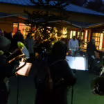 Das Bild zeigt die Musiker und einige der Gäste vor dem erleuchteten Pflanzraum.
